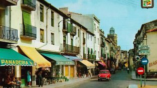 Postal del carrer Major dels anys 60 o inicis 70. A partir de la plaça Arias Comellas el carrer era de direcció única. El detall: la mítica Casa Gifreu i la Mercerai L. Vila entre les botigues ben identificades del carrer.