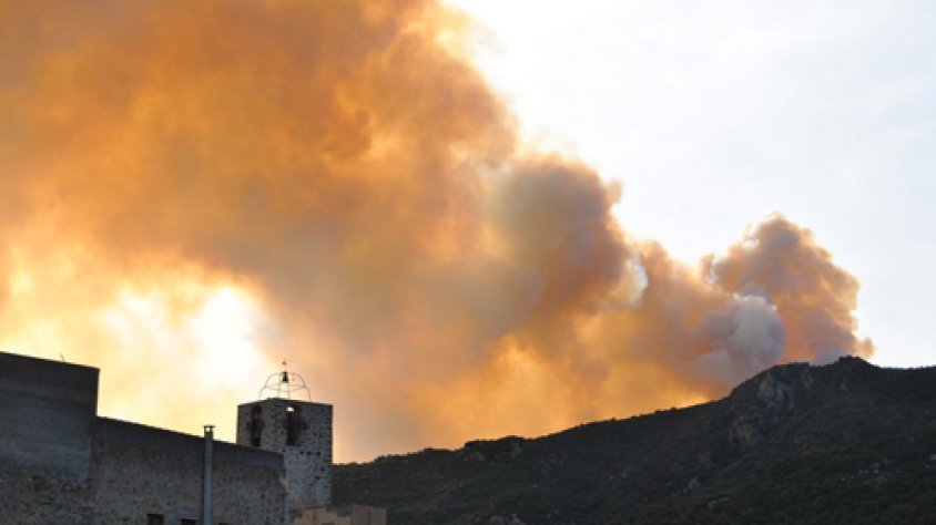 Cantallops a primer terme amb el campanar siluetejat sobre un cel ennuvolat per la cendra